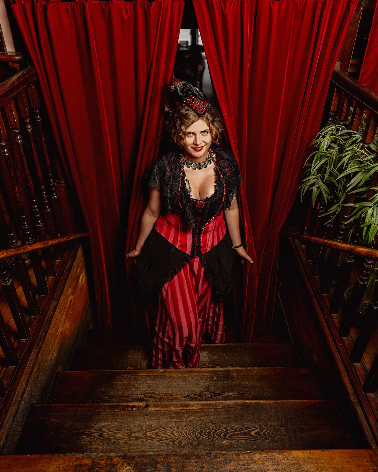 Madam ascending the staircase through the red velvet curtain